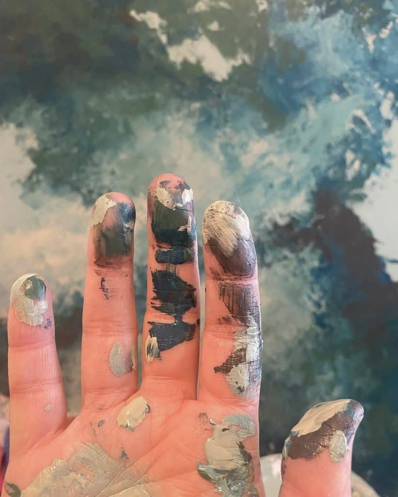 Local Artist Anne's painting hand against custom art piece in blue hues